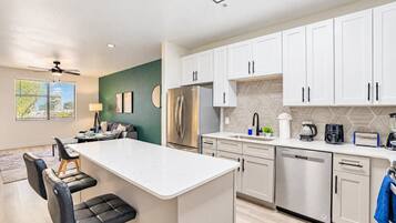 A modern kitchen with white cabinets, a central island, and a dining area with a sofa and chairs.