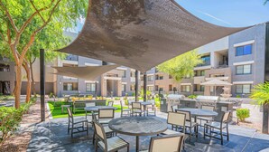 An outdoor patio area with round tables and chairs, surrounded by a low wall and trees. - Clean Westgate | Pool, Gym W/D Hot Tub Parking (Glendale)