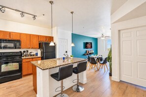 A modern kitchen with granite countertops, wooden cabinets, a black refrigerator, and a dining area with a blue accent wall. - Clean Westgate | Pool, Gym W/D Hot Tub Parking (Glendale)