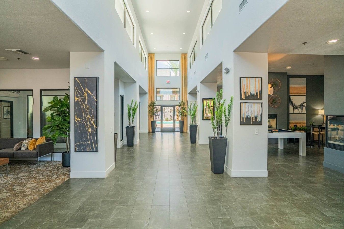 A spacious lobby with a high ceiling, a pool table, and potted plants.
