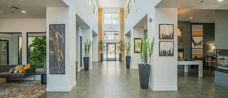 A spacious lobby with a high ceiling, a pool table, and potted plants.