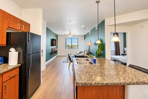 A kitchen with a granite countertop, wooden cabinets, a refrigerator, and a dining area with a table and chairs.