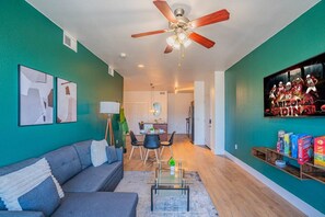 A living room with a grey sofa, a glass coffee table, a ceiling fan, and a dining area with chairs and a table. - Clean Westgate | Pool, Gym W/D Hot Tub Parking (Glendale)