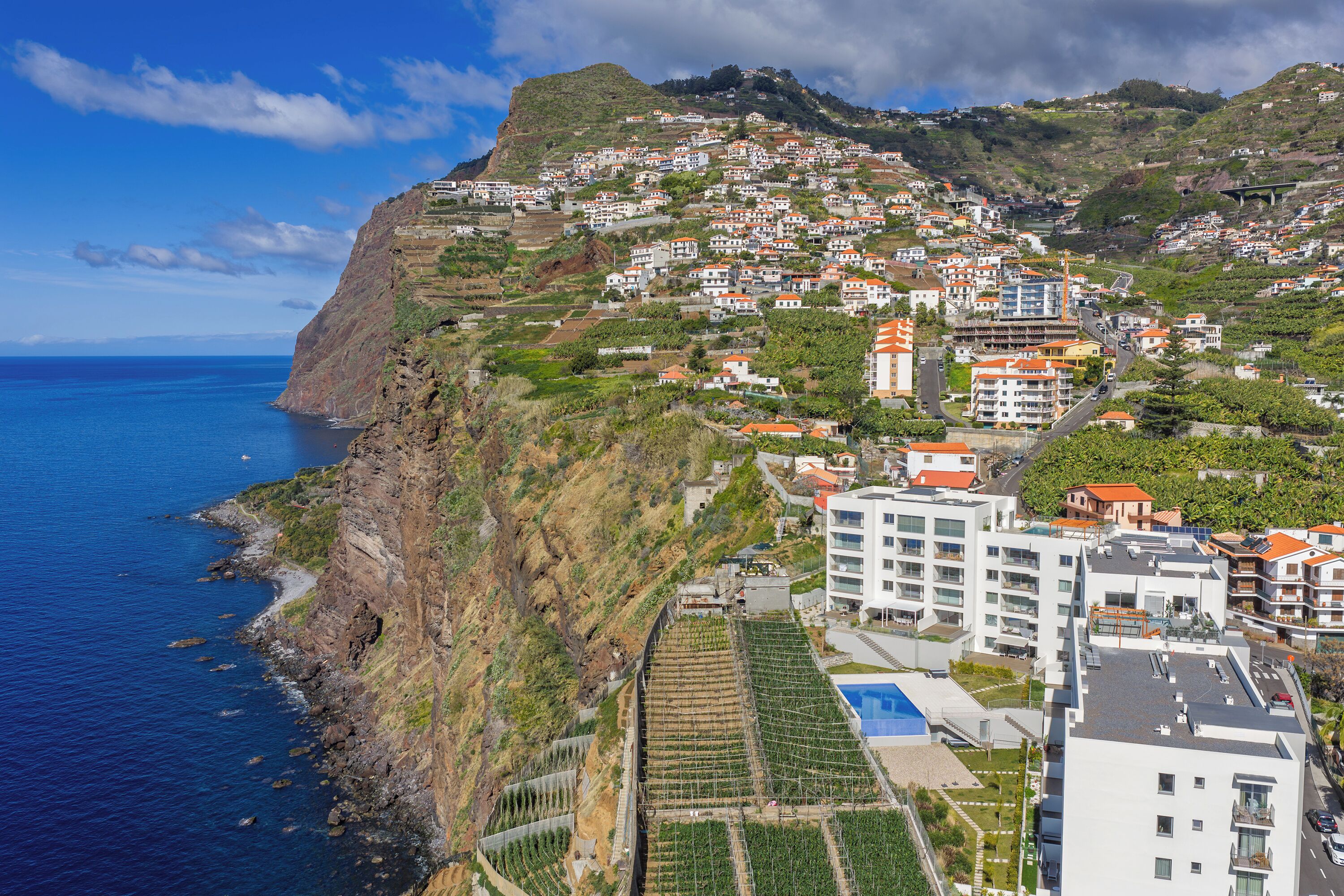 A coastal town with terraced houses, a clear blue sea, and a prominent hill.