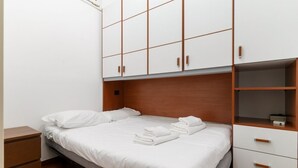 Un dormitorio con cama, cabecero de madera, armario blanco y mesita de noche.