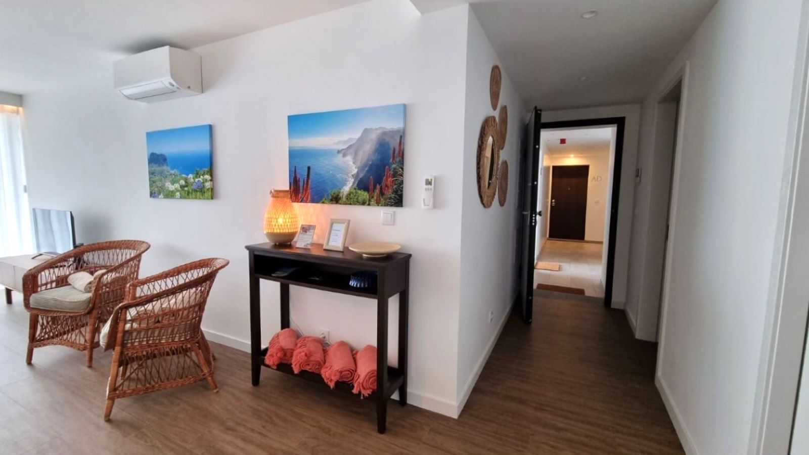 A modern living room with wicker chairs, a console table with a lamp, and two landscape paintings on the wall.