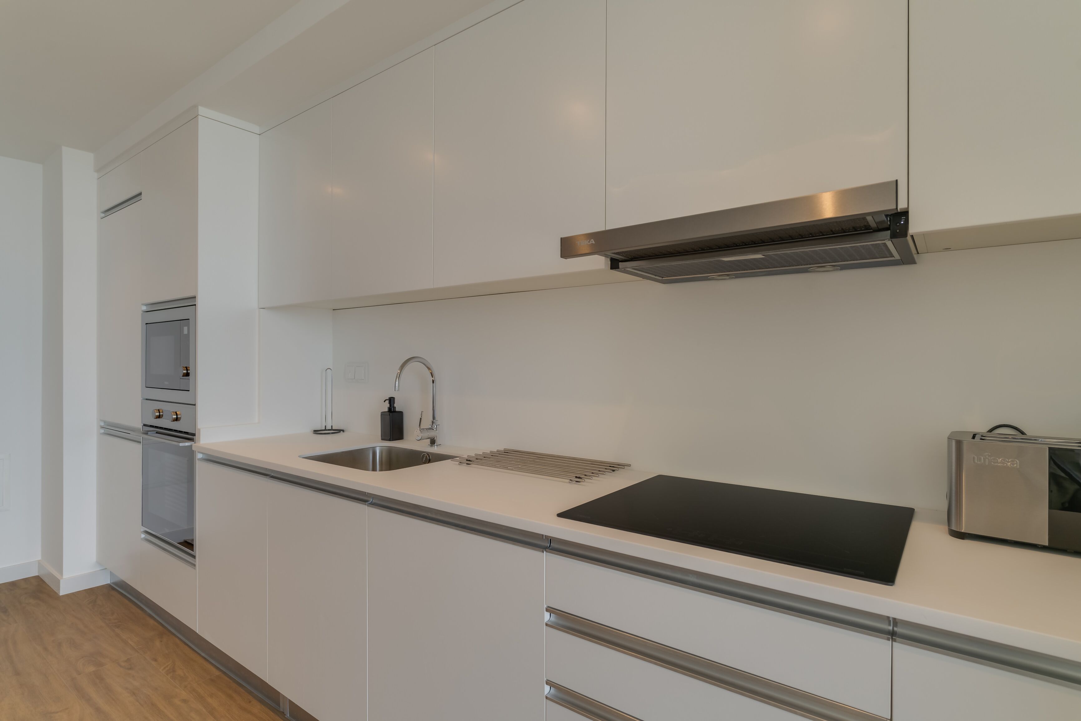 Une cuisine moderne avec des meubles blancs, des appareils en acier inoxydable et une plaque de cuisson à induction noire.