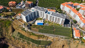 An aerial view of a hotel complex with multiple buildings, a parking area, and terraced vineyards.