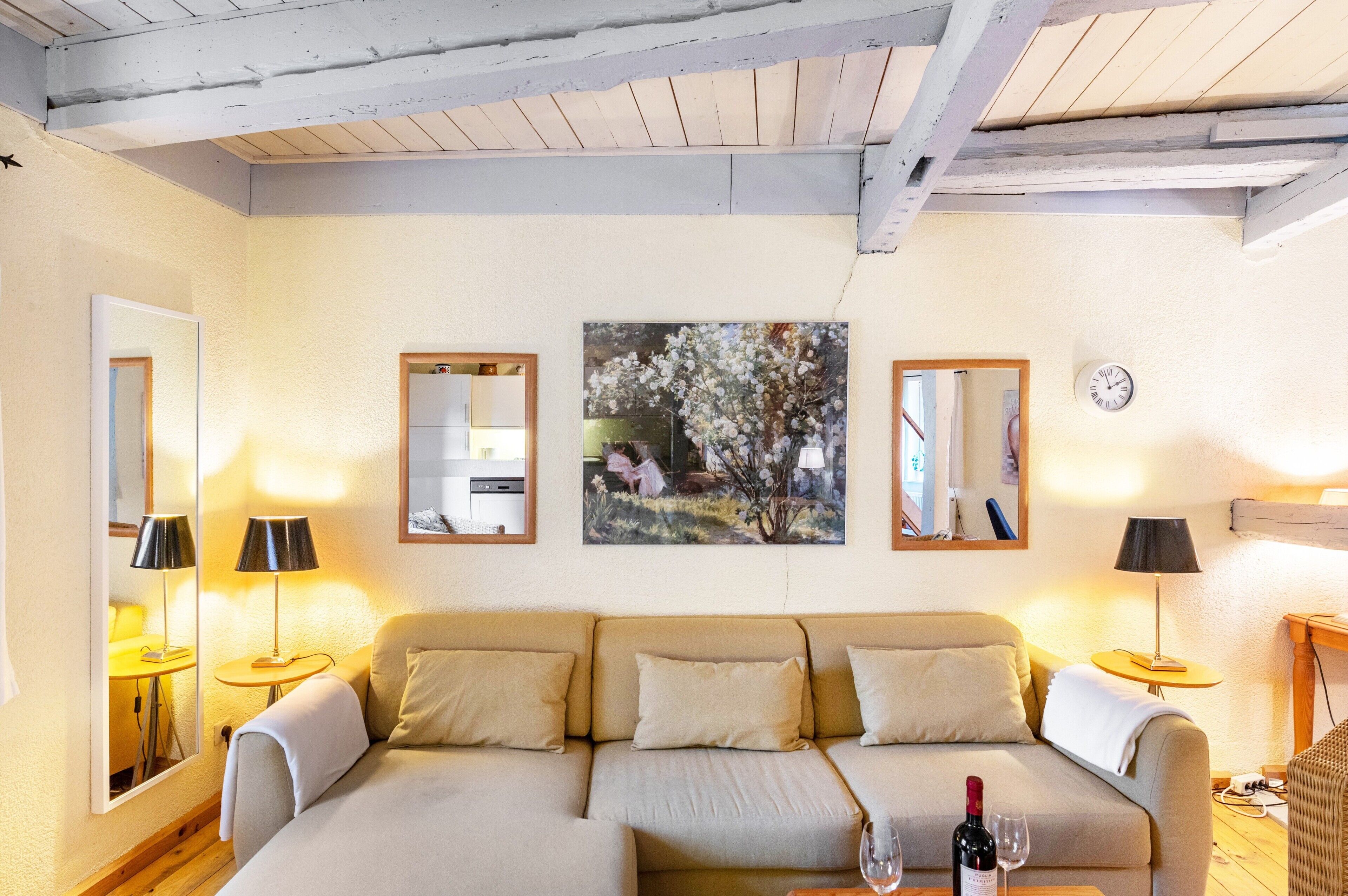 A cozy living room with a sofa, two lamps, a painting, and a clock on the wall.