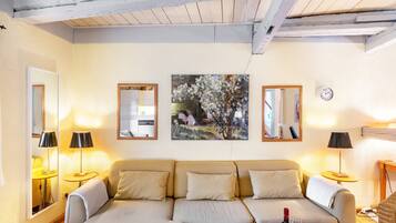 A cozy living room with a sofa, two lamps, a painting, and a clock on the wall.
