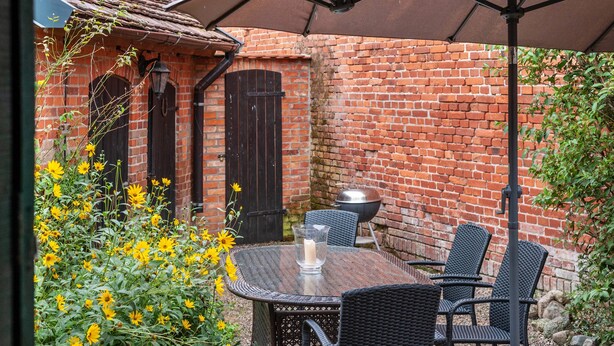 Un patio con una mesa, sillas, una parrilla y un muro de ladrillo.