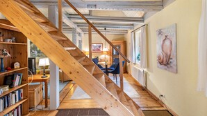 Una escalera de madera conduce a un comedor con una mesa y sillas, una estantería y un cuadro colgado en la pared.