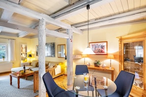 A cozy living room with a glass table, blue chairs, a sofa, and a dining area with a wooden cabinet.