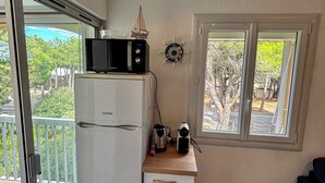 Una kitchenette compacta con refrigerador, microondas, hervidor de agua y cafetera sobre una encimera de madera.