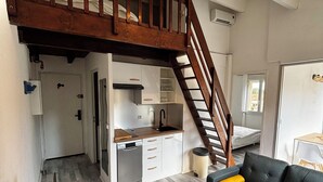 Un espacio habitable compacto con kitchenette, un sofá, una mesa de comedor y una escalera que sube a un nivel superior.