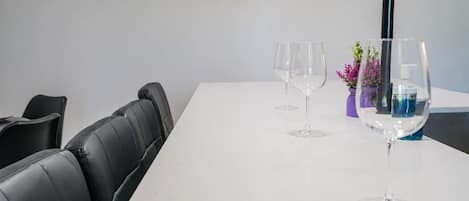 A white table with two empty wine glasses and a water glass, a black chair, and a potted plant with pink flowers.