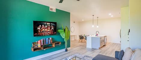 A modern living room with a teal accent wall, a mounted TV, a bookshelf, a coffee table, and a sofa.