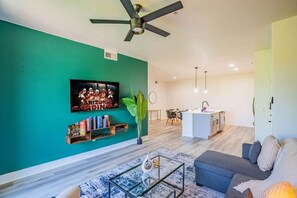 Ein modernes Wohnzimmer mit einer türkisfarbenen Akzentwand, einem Wand-Fernseher, einem Bücherregal, einem Couchtisch und einem Sofa.