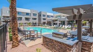 Un espace piscine avec des chaises longues, un coin barbecue et un mur en pierre.