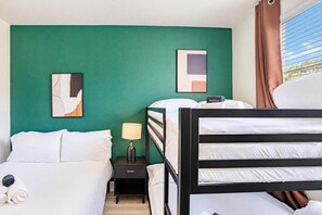 A hotel room with a bunk bed, a bedside table with a lamp, and artwork on the walls.