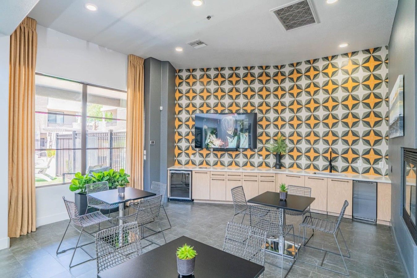 A modern interior with a dining area, kitchen, and a TV mounted on a geometric-patterned wall.
