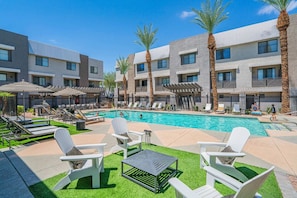 Un espace aménagé au bord de la piscine, avec des chaises longues, une piscine et un bâtiment à plusieurs étages doté de balcons.
