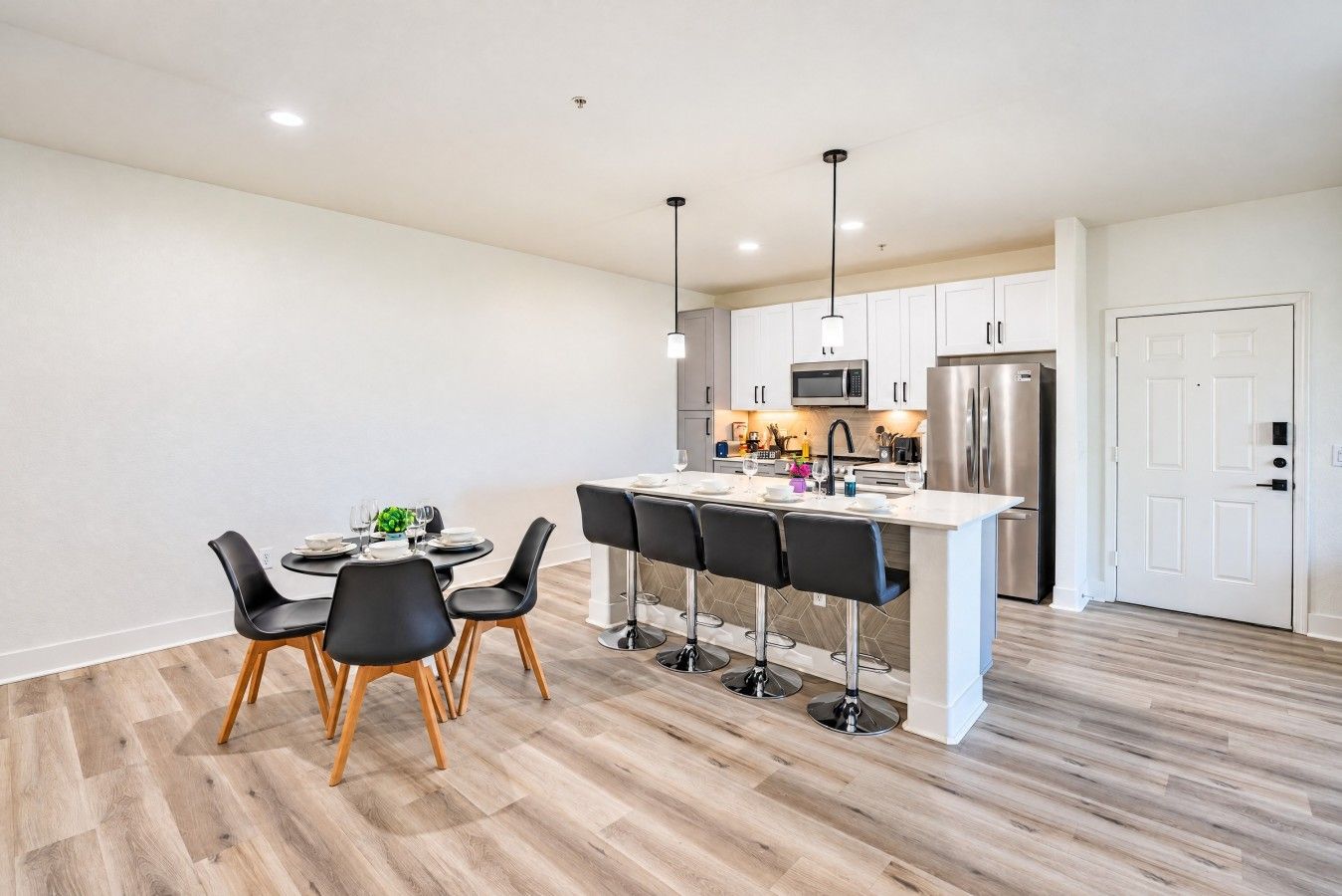 A modern kitchen with white cabinetry, stainless steel appliances, and a central island with bar stools.