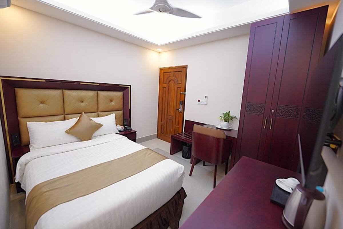 A hotel room with a large bed, a desk, a wardrobe, and a ceiling fan.