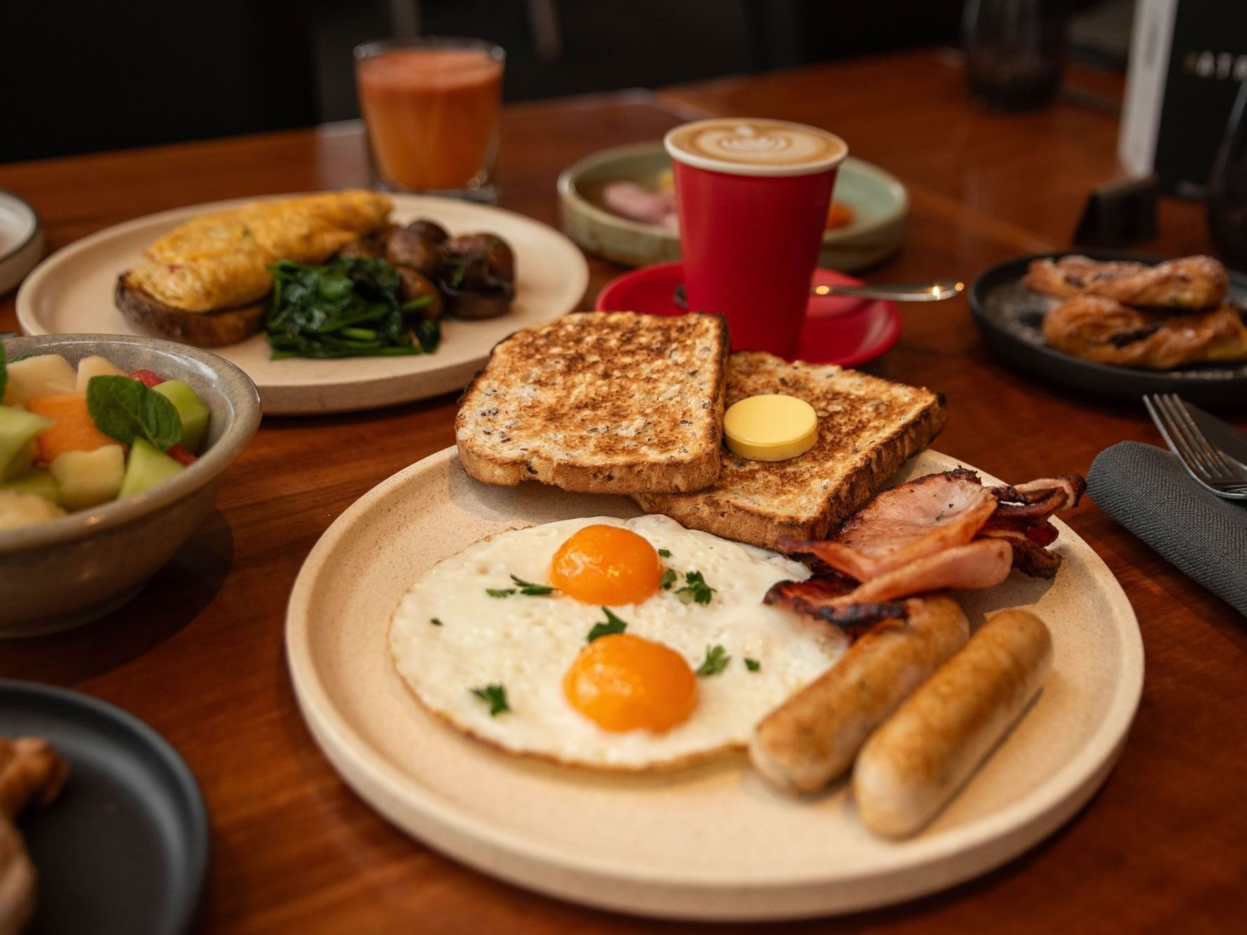 A breakfast setting with toast, eggs, sausages, and a fruit bowl.