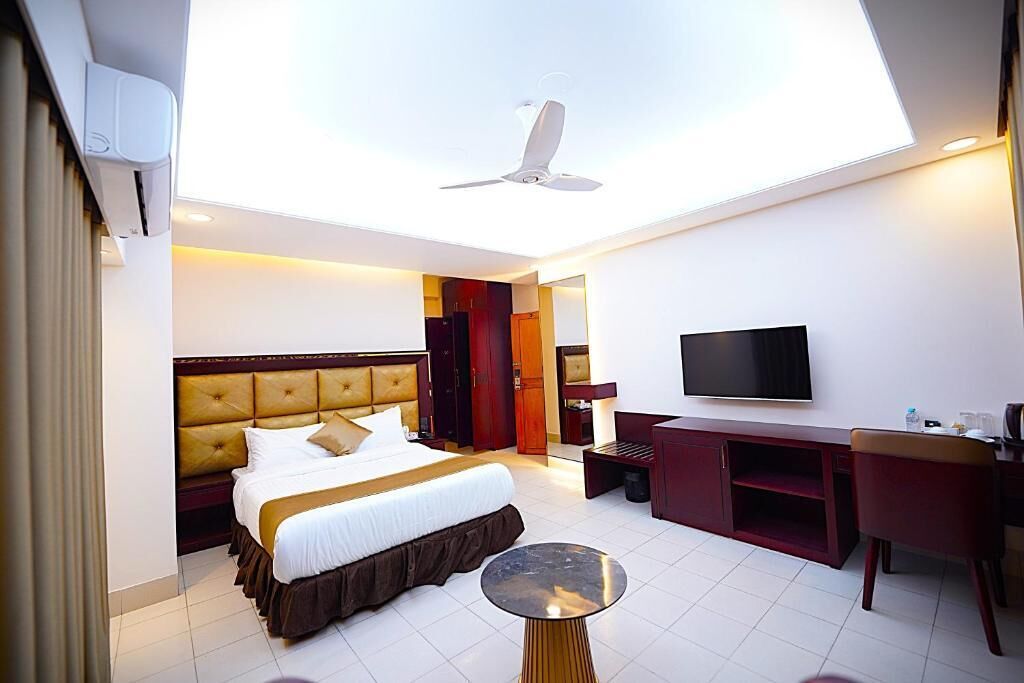 Een hotelkamer met een bed, bureau, televisie en plafondventilator.