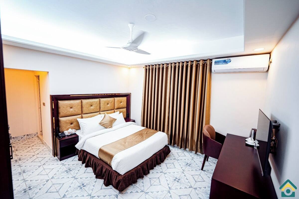 A hotel room with a bed, a desk, a chair, a ceiling fan, and a window with curtains.