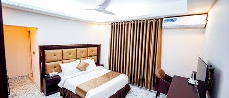 A hotel room with a bed, a desk, a chair, a ceiling fan, and a window with curtains.