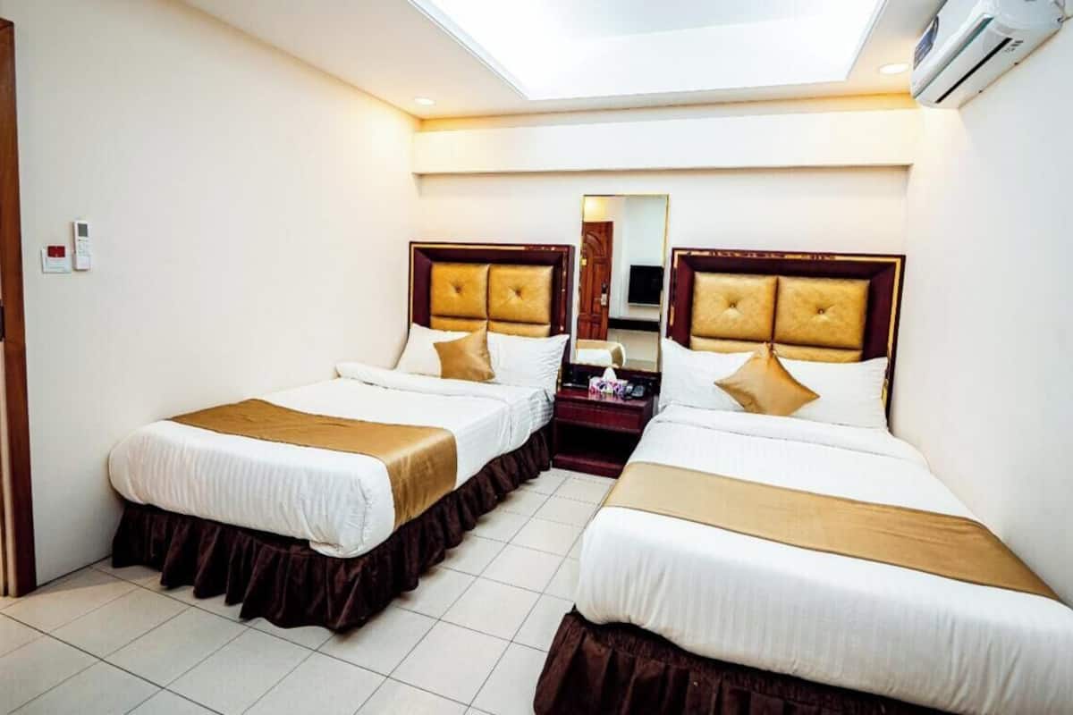 A hotel room with two beds, a mirror, a bedside table, and an air conditioning unit.