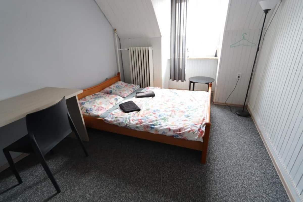 A bedroom with a bed, a desk, and a chair.