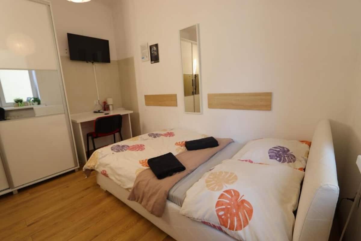 A bedroom with a bed, a desk, a chair, a TV, and a mirror.