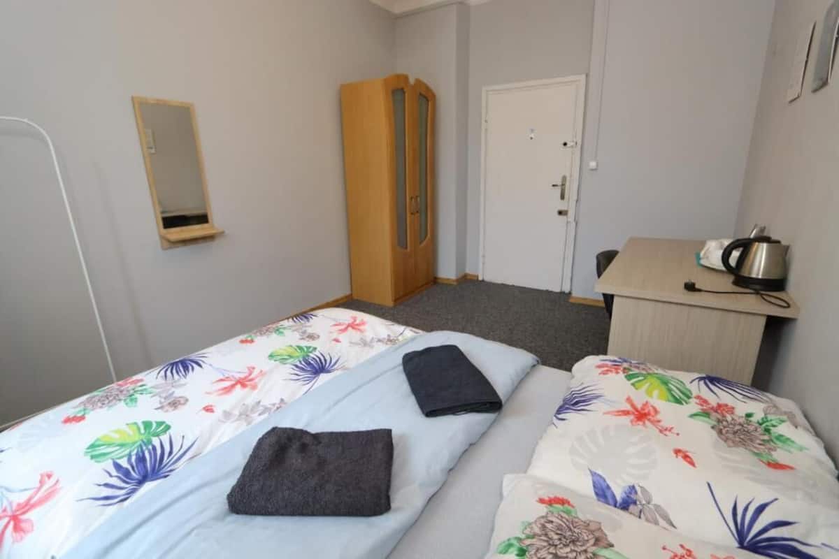 A room with two beds, a wardrobe, a desk with a kettle, and a mirror on the wall.