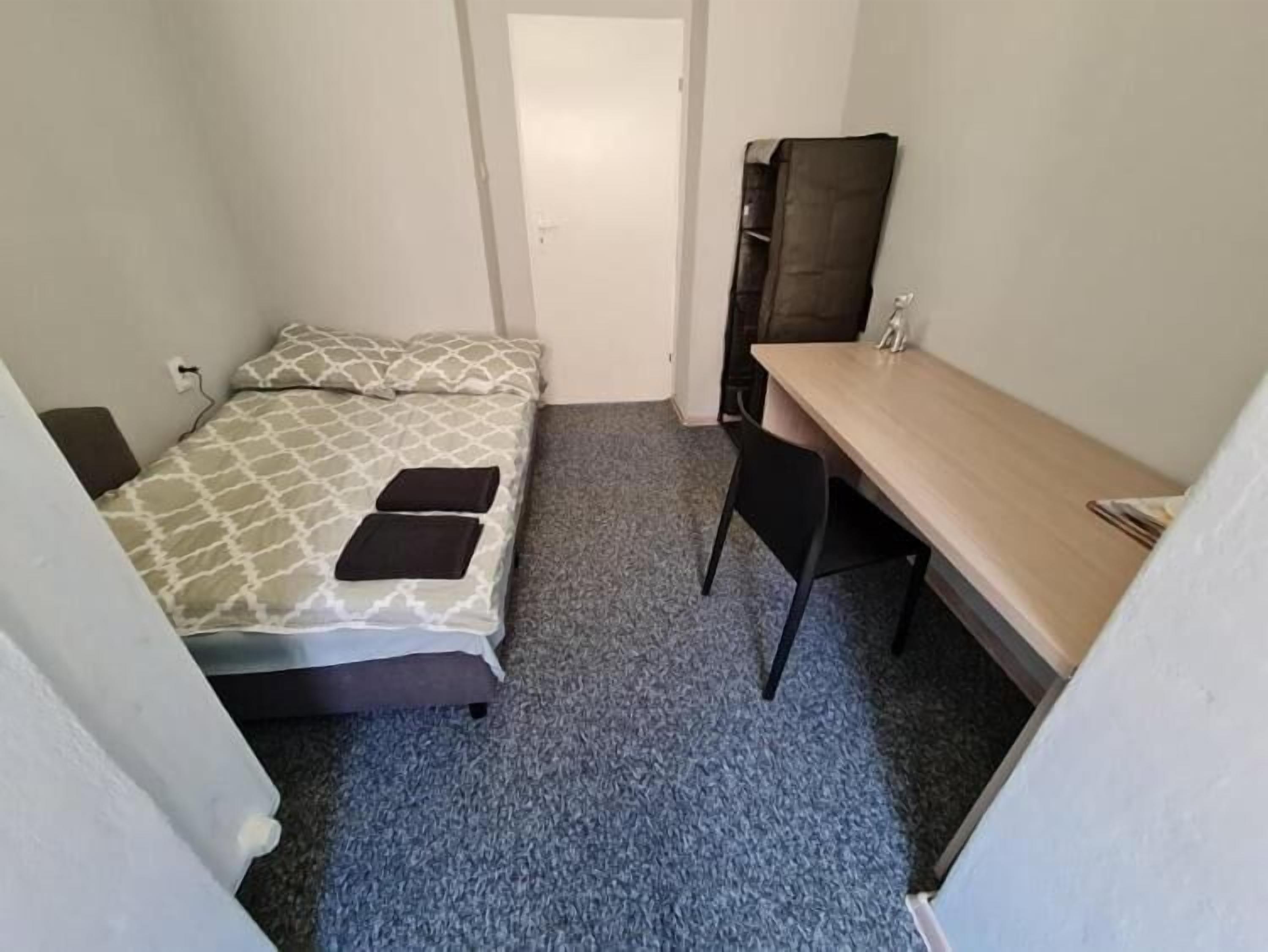 A small, compact room with a single bed, a desk, and a chair.