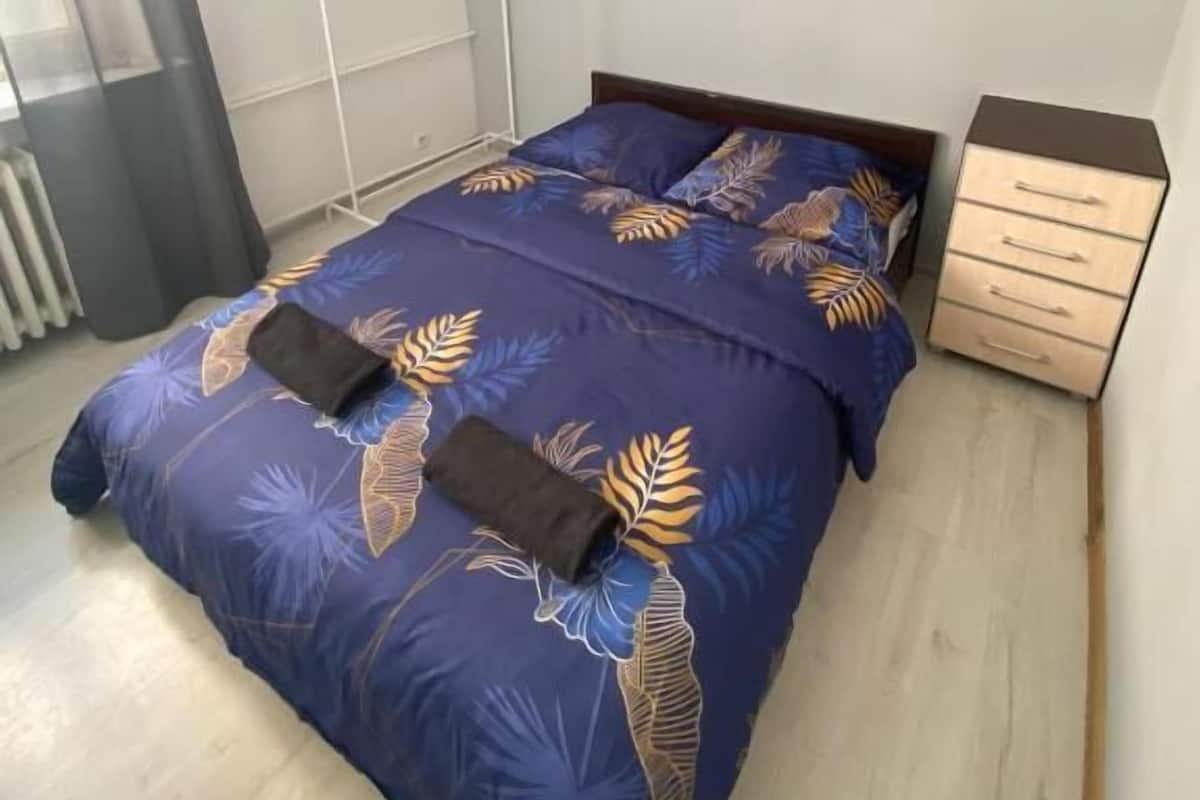 A bedroom with a bed, a nightstand, a radiator, a hanging light fixture, and a painting on the wall.