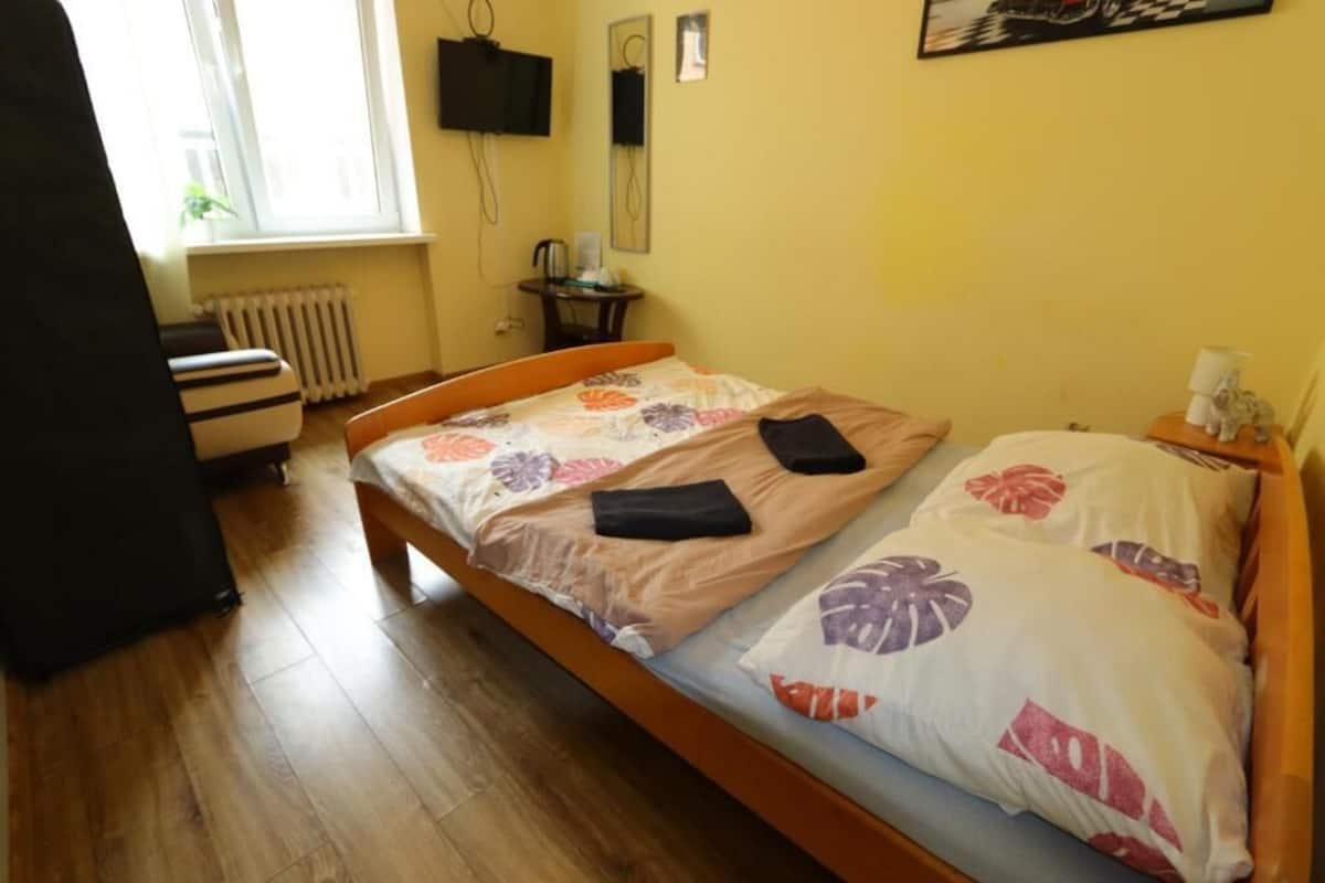 A bedroom with a wooden bed, a radiator, a television, and a small table with a lamp.