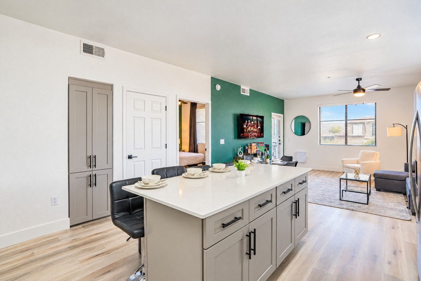 A modern kitchen with a central island, a dining area with chairs, a living room with a sofa, and a view of the outdoors.
