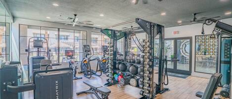 A gym with cardio equipment, weightlifting stations, and a ceiling fan.