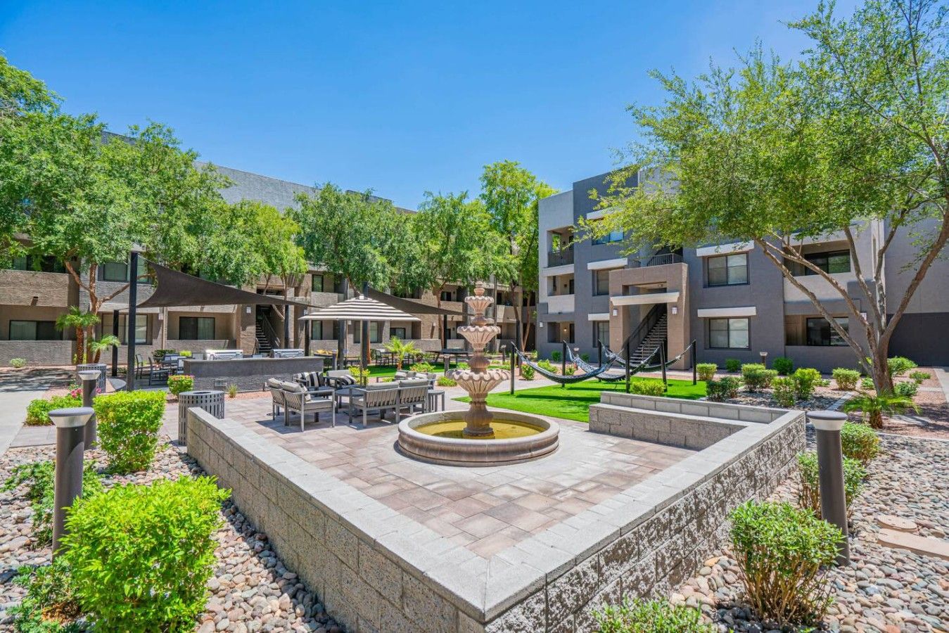 A courtyard with outdoor seating, a central fountain, and modern buildings in the background.