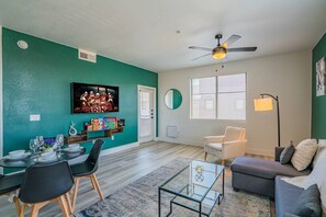 A living room with a teal wall, a ceiling fan, a dining area with chairs and a table set, a sofa, and a floor lamp. - Chic Stay Near Westgate | Pool, Gym, Parking & W/D (Glendale)