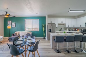 Une cuisine moderne avec des meubles blancs, un îlot central doté de tabourets de bar et un coin repas avec une table dressée pour quatre personnes.