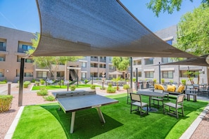 Un espace extérieur aménagé en terrasse, avec une table de ping-pong, des sièges et un coin ombragé.