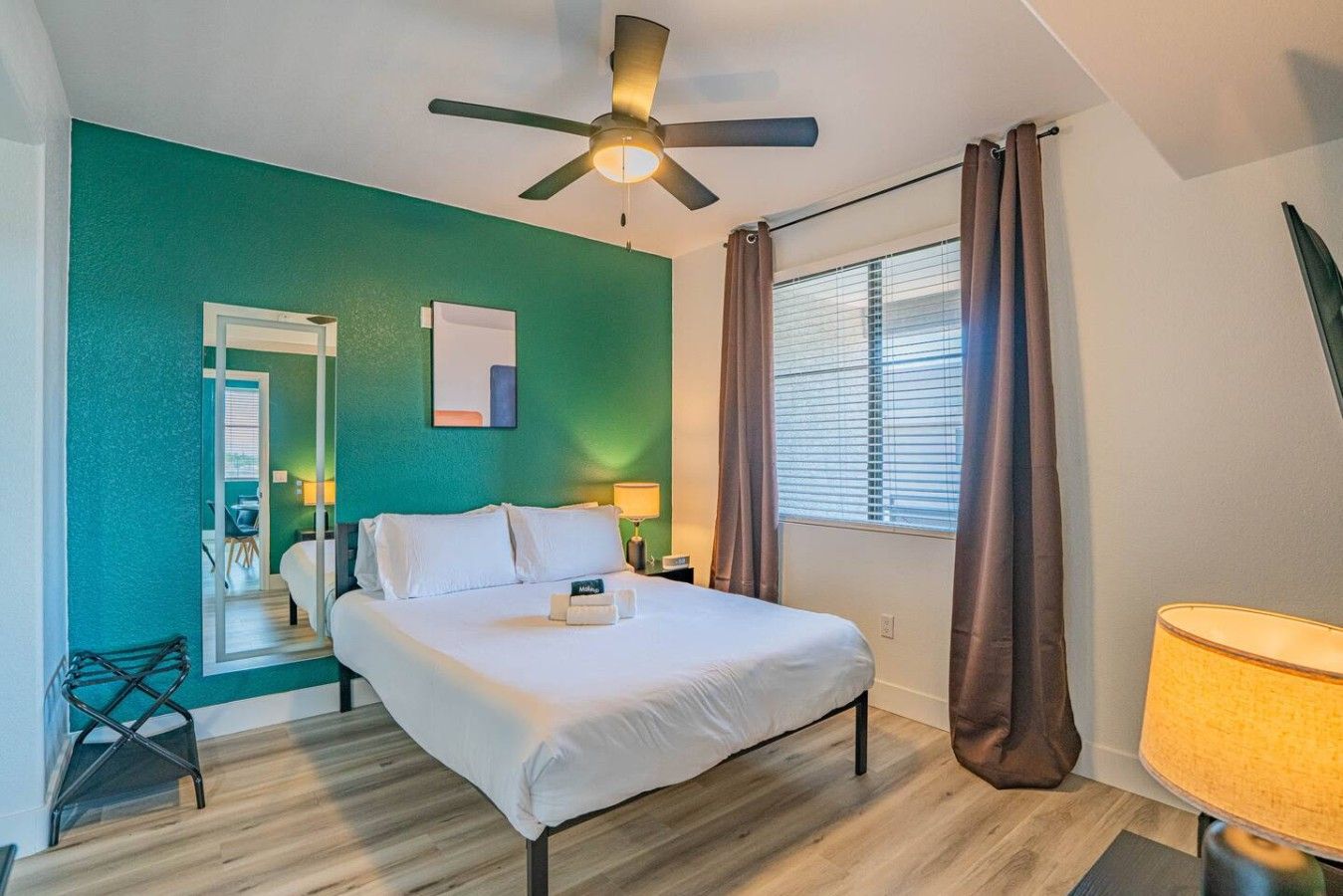 Une chambre à coucher avec un lit, un ventilateur de plafond, une fenêtre avec des rideaux et une table de chevet.