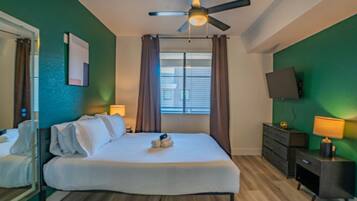 Une chambre d’hôtel avec un lit, un ventilateur de plafond, un téléviseur fixé au mur et une fenêtre avec des rideaux.