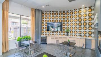 Un intérieur moderne comprenant un coin repas, une cuisine et un téléviseur fixé à un mur orné d’un motif géométrique.