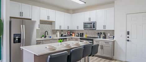 A modern kitchen with white cabinets, a central island with bar stools, a built-in microwave, and a stainless steel refrigerator.