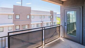 Un balcon avec une balustrade en métal, une porte avec une fenêtre et une vue sur les bâtiments adjacents.